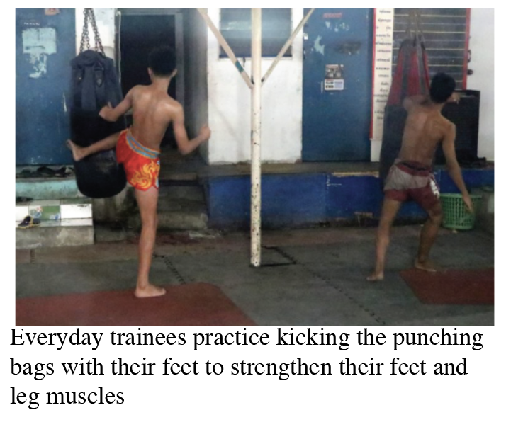 Two Muay Thai trainees hitting punching bags with their legs to strengthen their legs.